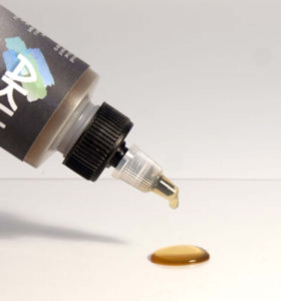 4oz. Akua Liquid Pigment Extender pouring from a bottle with a drop on a surface.