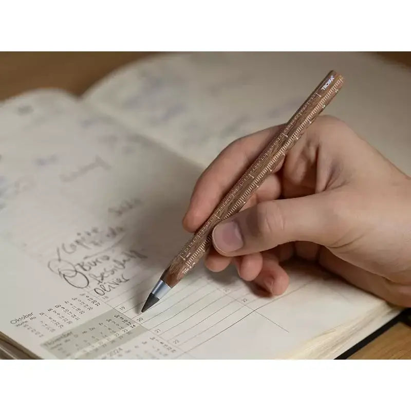 Person using a Construction Endless Walnut Pencil on an open planner, showcasing elegant design and functionality.