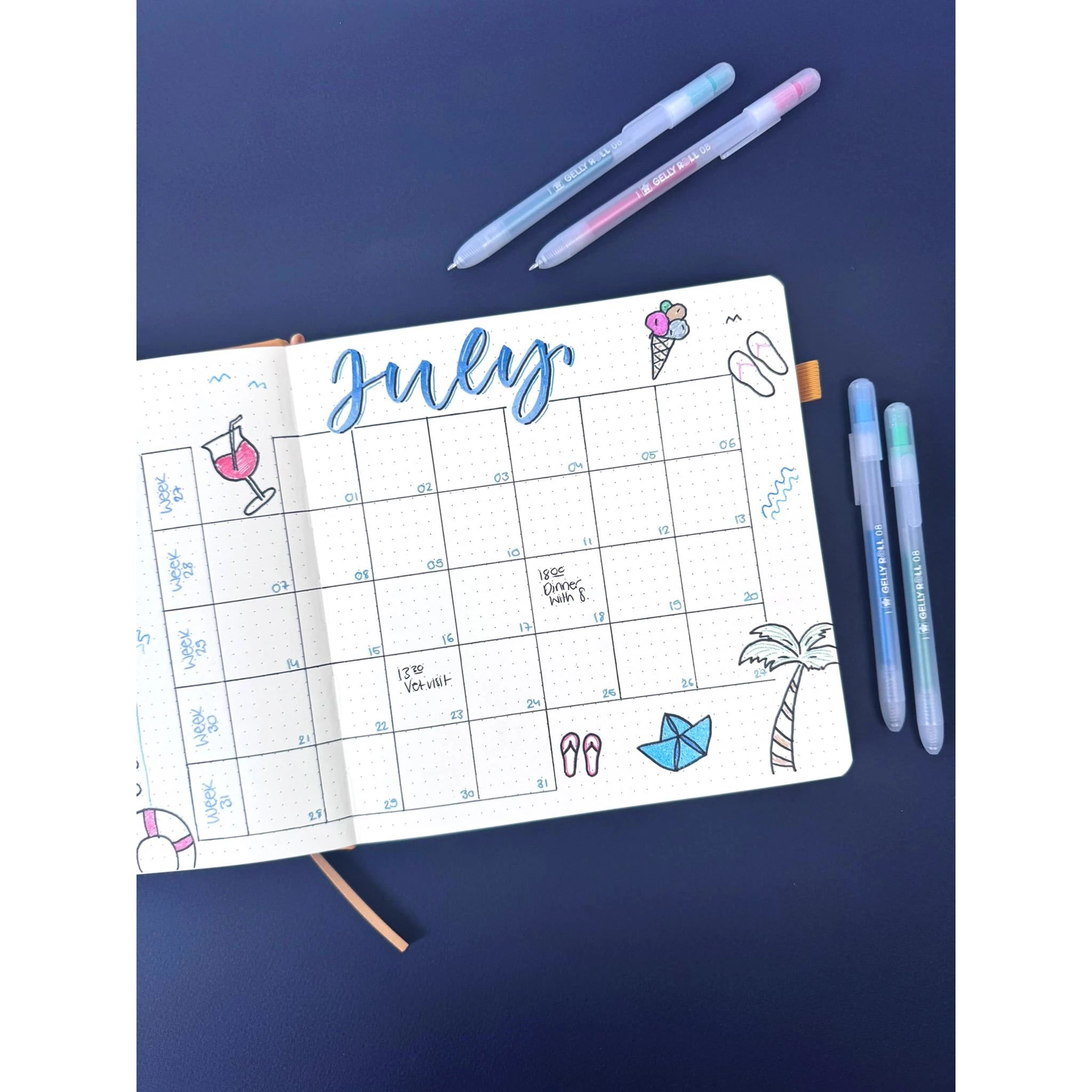 July planner with beach-themed doodles, featuring Gelly Roll Stardust glitter gel pens in various colors on a navy background.