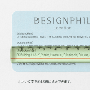 Midori Lens Ruler 15cm – Yellow lying on a blue card, showing magnified text with 1.5× enlargement.
