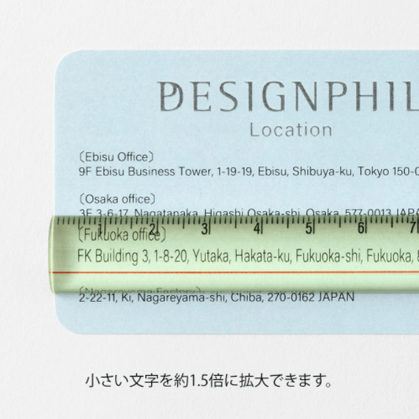 Midori Lens Ruler 15cm – Yellow lying on a blue card, showing magnified text with 1.5× enlargement.
