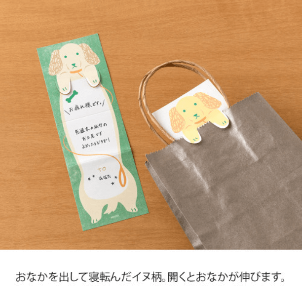 Midori Memo Stretchy Dog fold-out memo pad with dog design hanging on a gift bag, showcasing extra writing space for messages.