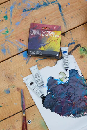 W&N Artists' Oil Colour 5x37ml Tubes Primary Set on a rustic wooden table with mixed colors on a palette.